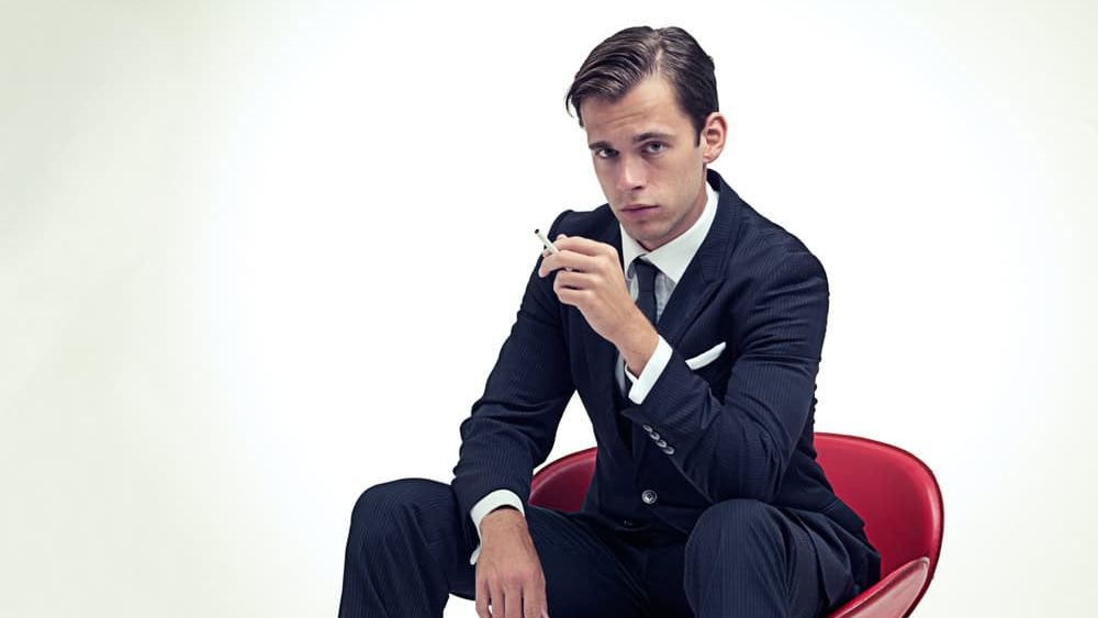 Suave smoker. A studio portrait of a handsome young gentleman in a pinstripe suit sitting on a chair.