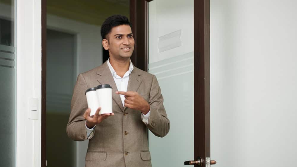 Smiling businessman bringing take-out coffee for himself and colleague in the morning