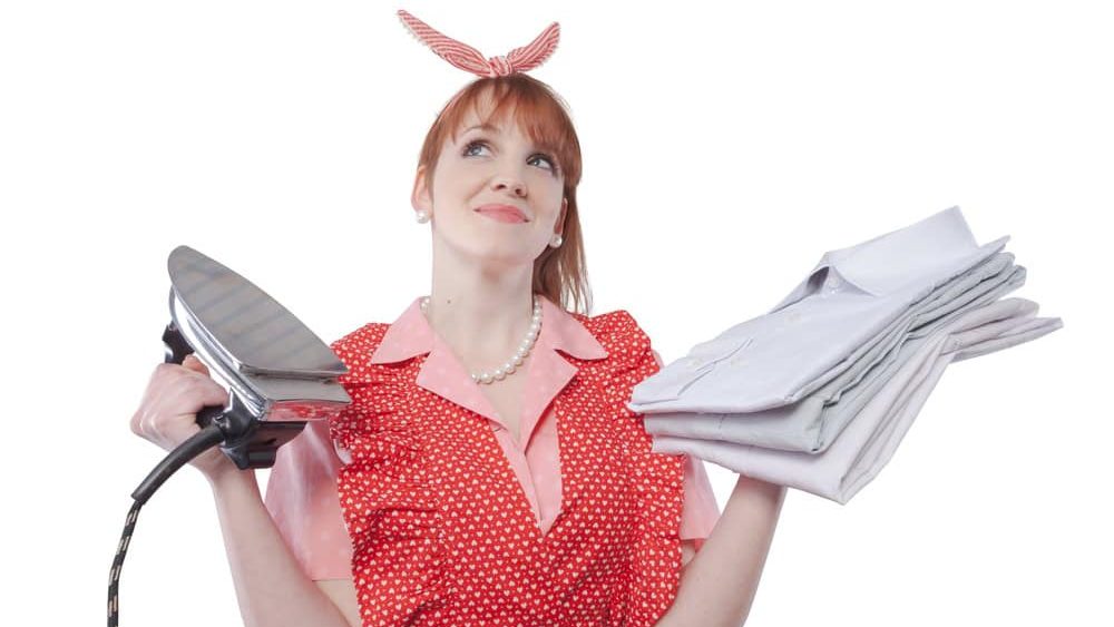 Vintage style efficient housewife holding an iron and a pile of clean ironed shirts