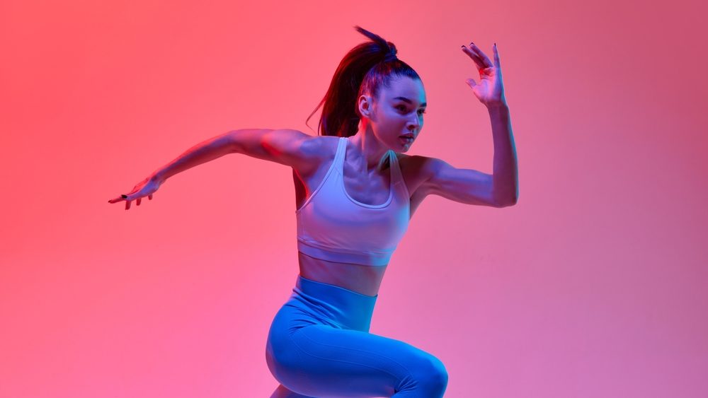 Developing speed. Young girl, professional athlete, runner in motion, training over pink studio background in neon light. Concept of sportive lifestyle, health, endurance, action and motion. Ad