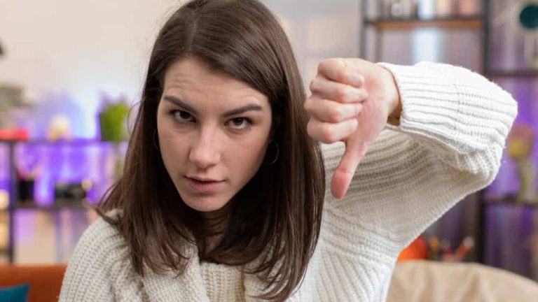 Dislike. Portrait of upset woman showing thumbs down sign gesture, expressing discontent, disapproval dissatisfied bad work at modern home apartment indoors. Displeased girl in living room on sofa