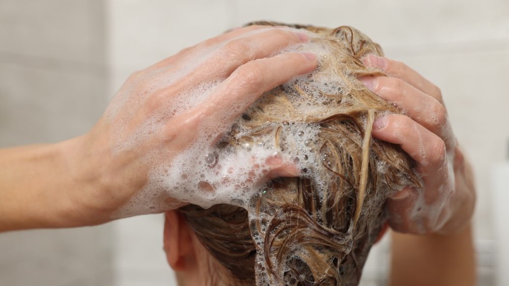Woman washing hair with shampoo indoors, closeup