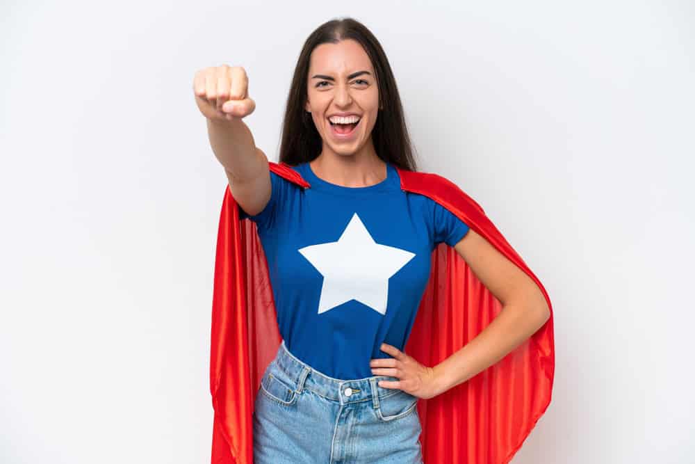 Young caucasian woman isolated on white background in superhero costume with proud gesture
