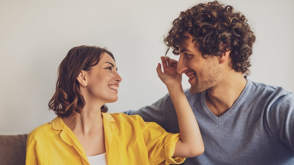Portrait of young happy couple in love. Woman is playing with man's curly hair.