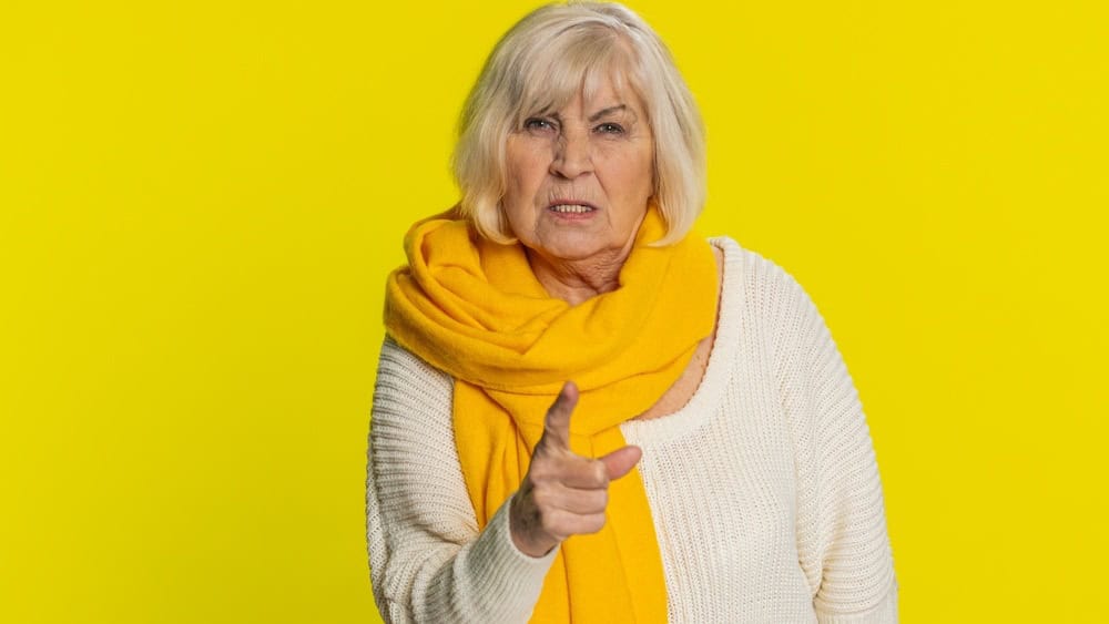 Quarrel. Displeased aggressive unhappy senior old woman gesturing hands with irritation and displeasure, blaming scolding for failure asking why this happened. Elderly grandmother on yellow background
