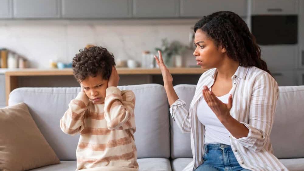 Stubborn Child. Offended black boy covering ears, not to hear mother's scolding, emotional african american woman arguing with her preteen son, family of two quarelling while sitting on couch at home