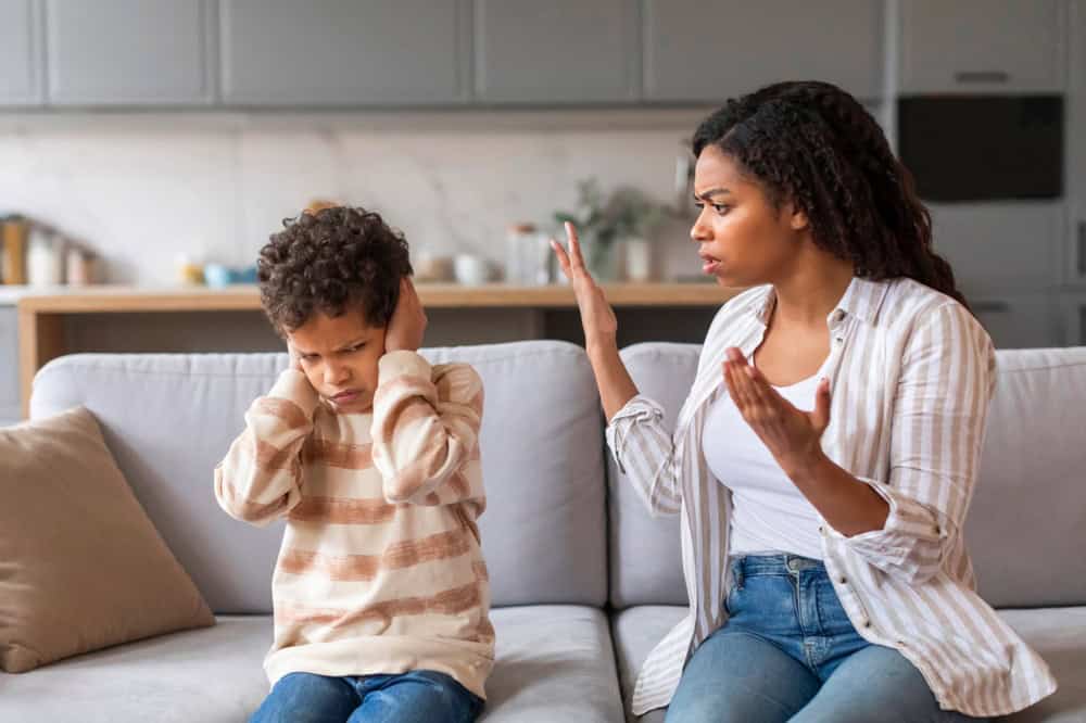 Stubborn Child. Offended black boy covering ears, not to hear mother's scolding, emotional african american woman arguing with her preteen son, family of two quarelling while sitting on couch at home