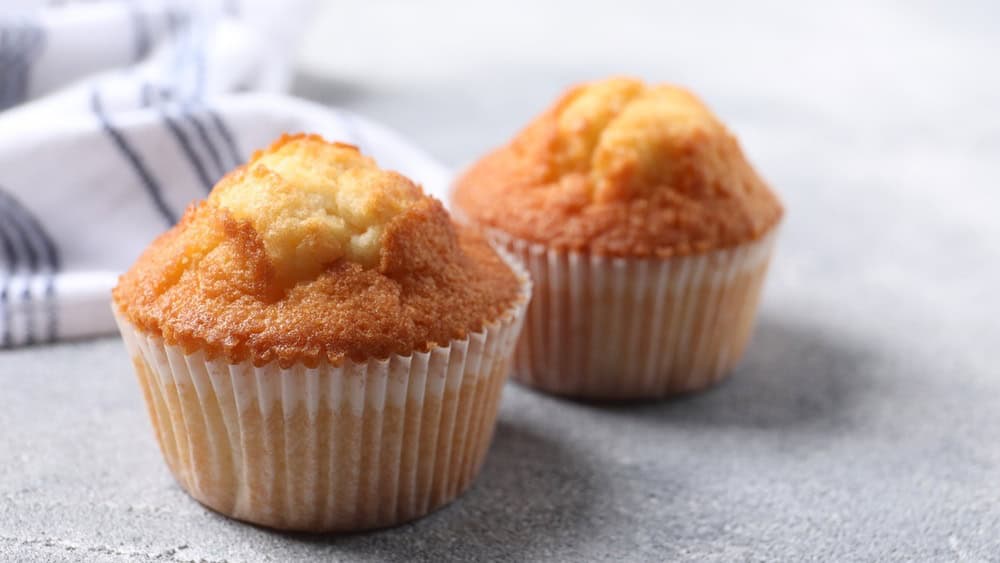 Delicious sweet muffins on light grey textured table, closeup. Space for text
