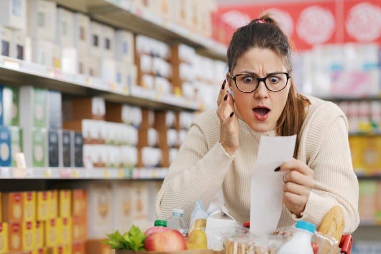 Shocked woman checking a long grocery receipt at the supermarket, expensive grocery and inflation concept