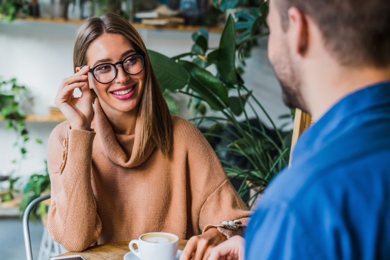 Attractive couple drinking coffee on date in cozy coffee shop. Caucasian man and woman colleagues business partners have meeting in modern cafe, sitting in restaurant with green plant on background