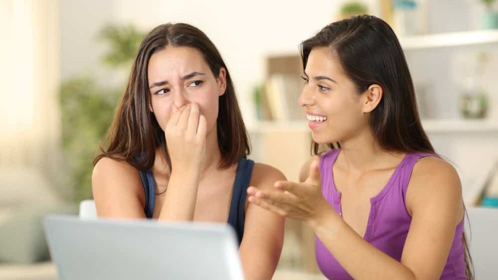 Woman with bad breath talking to a disgusted friend at home