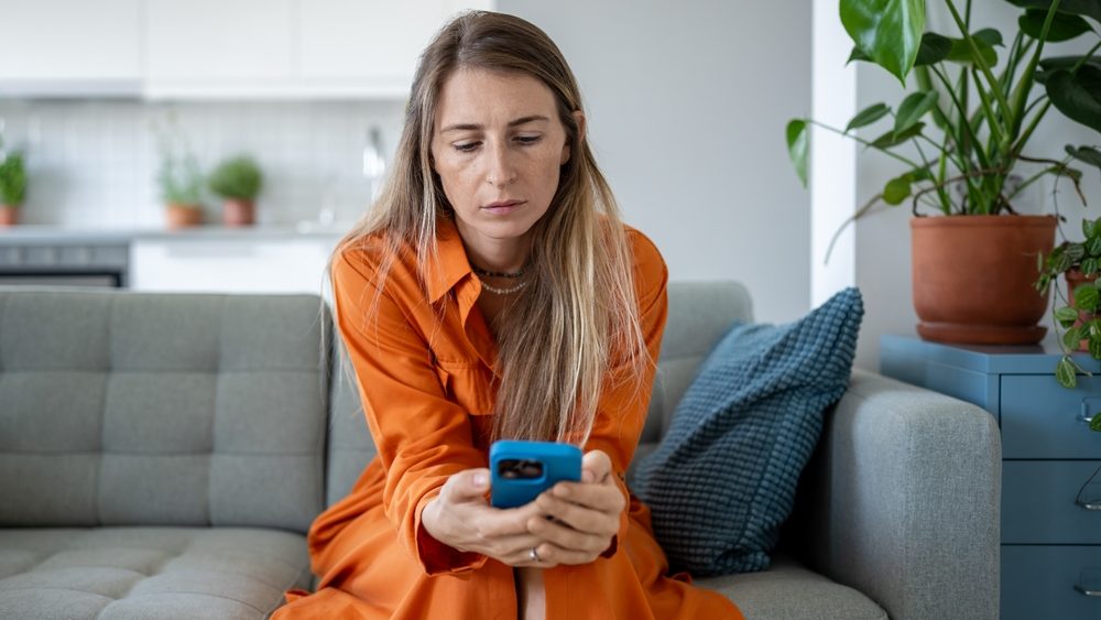 Sad woman holding mobile phone in hands, waiting for call or message. Frustrated female reading news, looking with strained uncertainty at smartphone with bad thoughts in head, loss of connection.