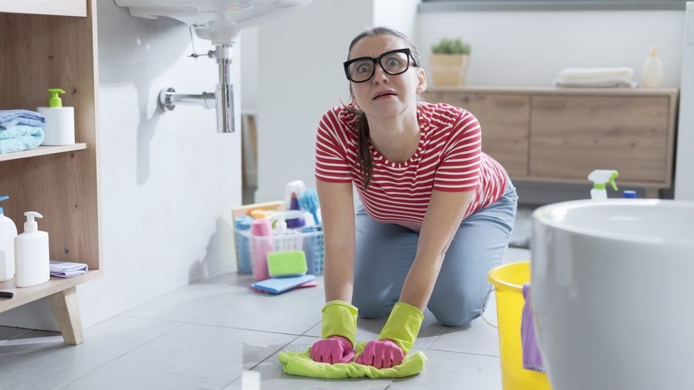 Frustrated woman cleaning her home and drying a water leak on the floor