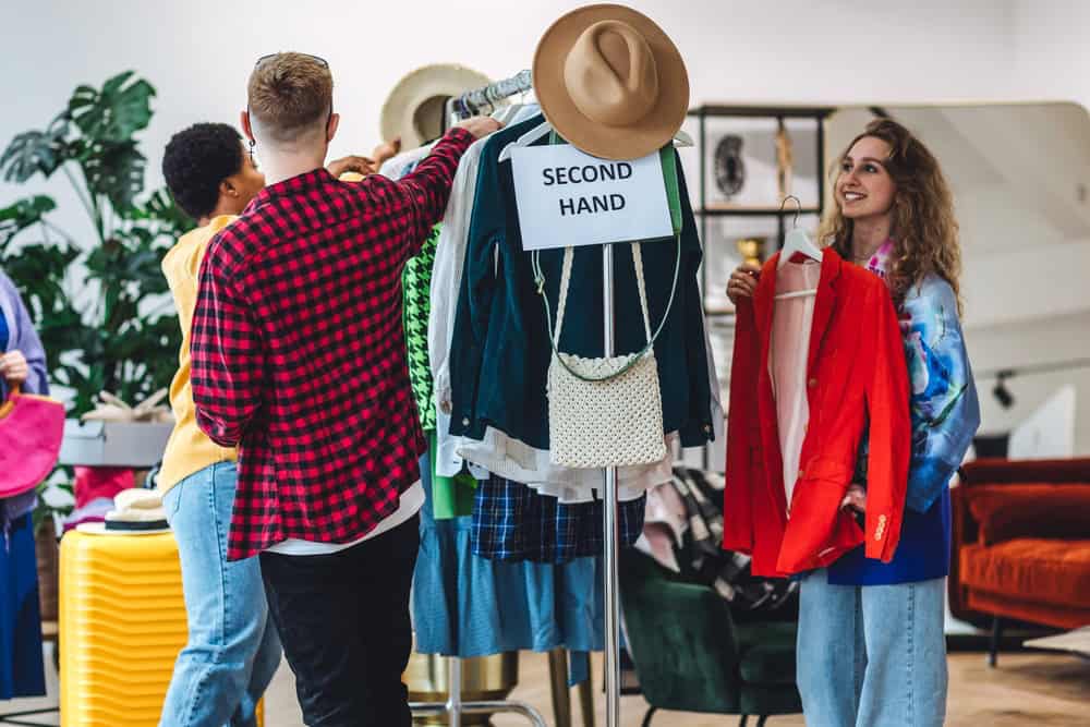 Students, young attractive people shopping in secondhand store, trying vintage clothes, bargain hunting. Sustainable lifestyle of generation z, eco friendly conscious consumerism, consignment stores