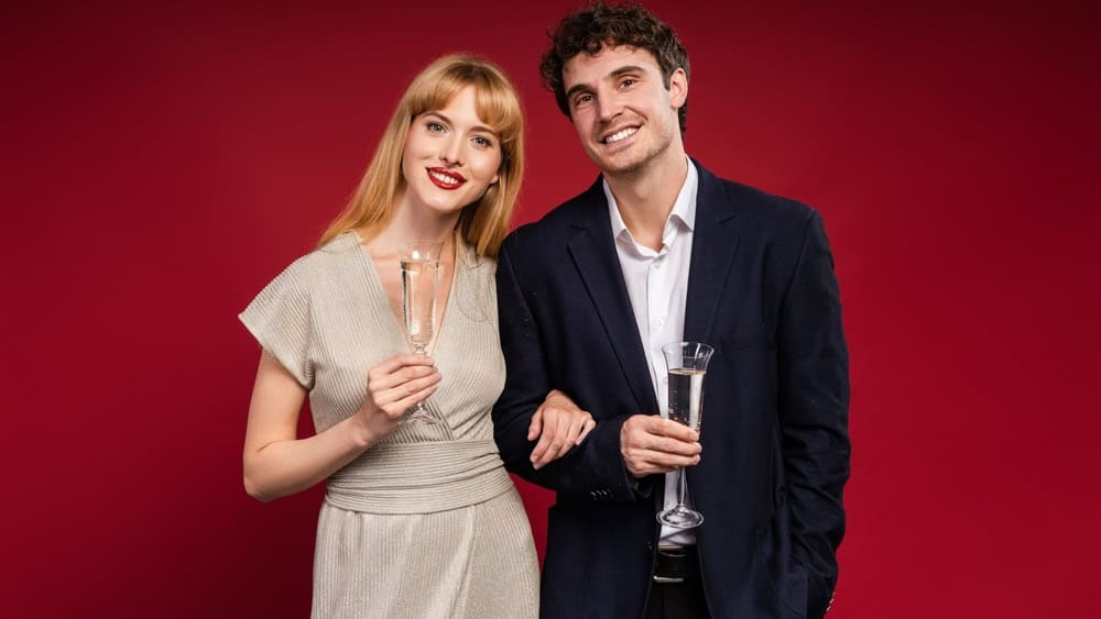 Stylish couple celebrating a special occasion, dressed up for a glamorous party, holding champagne glasses against a vibrant red background, radiating happiness and love