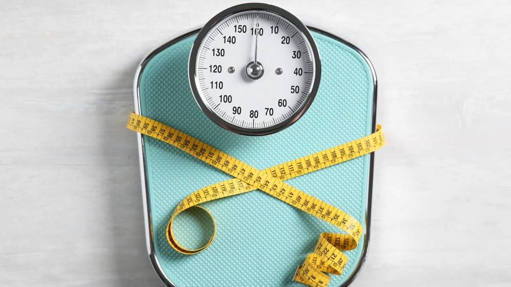 Scale tied with measuring tape on light wooden background, top view