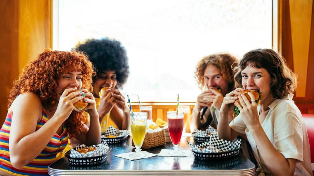 Multiethnic group of friends having meal at 80s vintage diner restaurant - Multiracial young people bonding and having fun, eating in an american fast food burger house