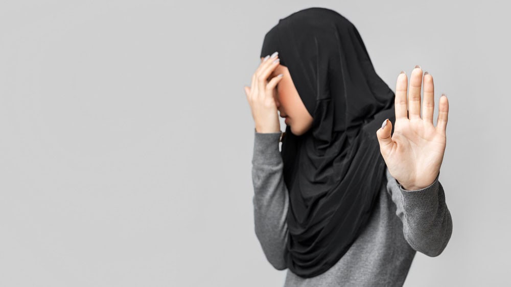 Domestic Violence Among Muslim Women Concept. Arabic woman in hijab making stop gesture and covering her face over gray studio background.