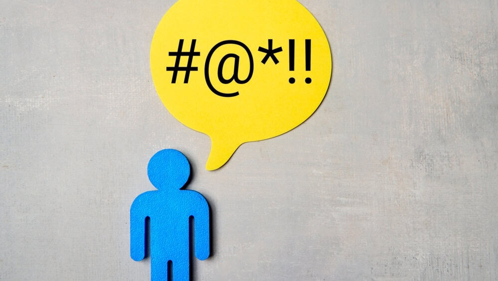 Blue figure with a yellow speech bubble containing symbols on a grey background. Profanity, foul language concept.