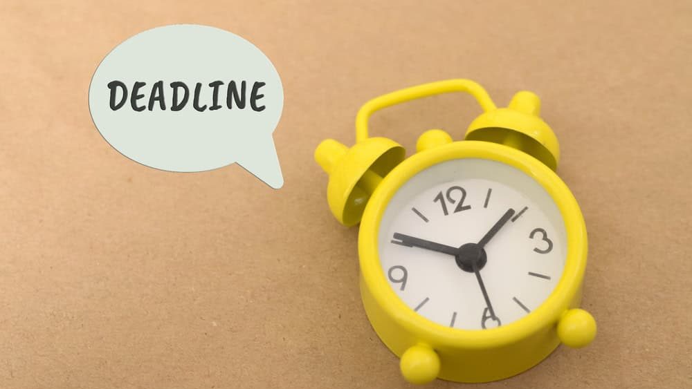 Bright yellow alarm clock with a speech bubble saying 'DEADLINE' on a brown background.