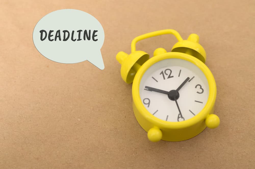 Bright yellow alarm clock with a speech bubble saying 'DEADLINE' on a brown background.