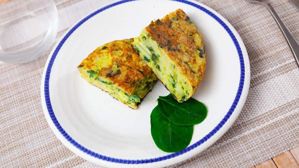 There are two pieces of lush baked omelet with spinach on plate, egg souffle is covered with delicate crispy crust and ready to eat