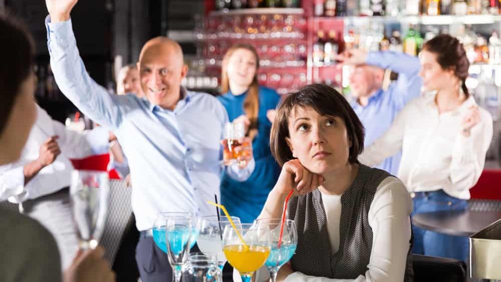 Bored adult woman sitting at table, having no fun at corporate party in bar