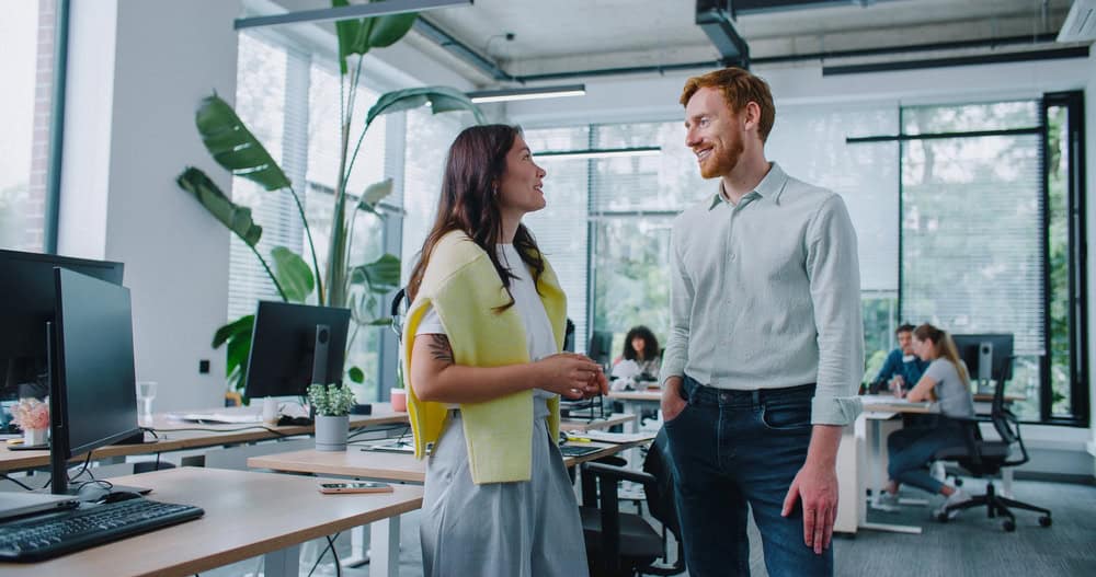Satisfied mixed-raced workers talking with each other during free time at work. Pretty woman telling stories about funny situation in working day. Man widely smiling and giving high-five to coworker.