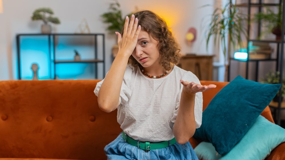 Face palm. Shame on you. Upset woman making disrespect gesture, feeling bored disappointed in fail results bad news. Portrait of girl at home living room sitting on couch sofa. Lifestyles. Lifestyles.