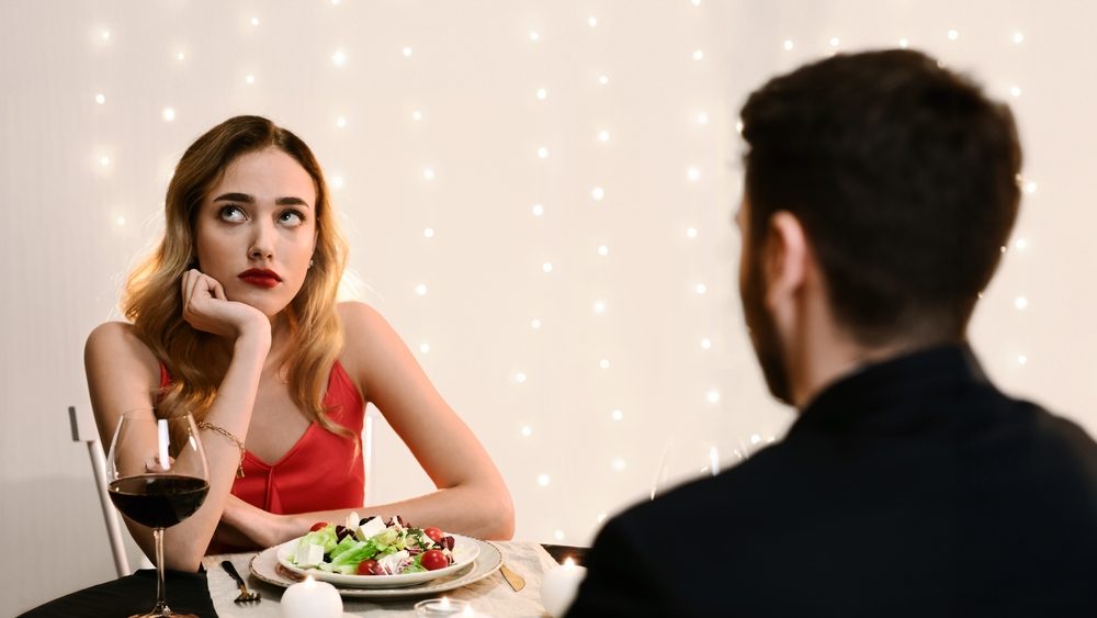 Unsuccessful Date. Young woman feeling bored at dinner in restaurant, looking away with disappointed face expression, selective focus
