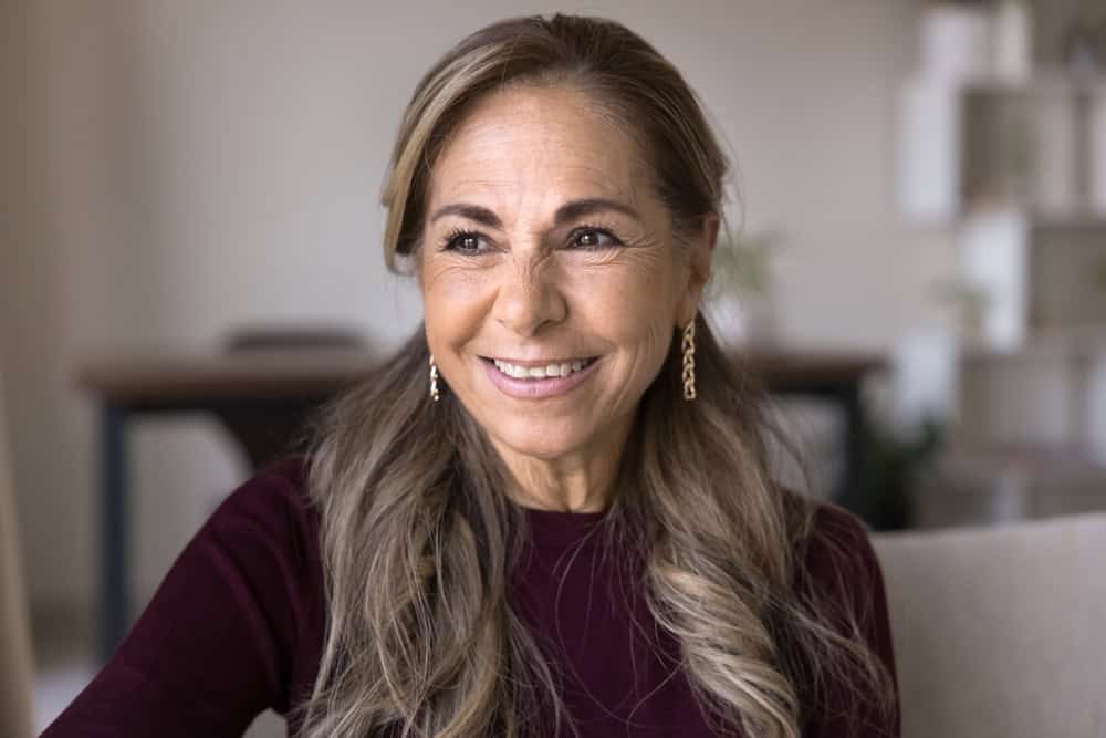 Happy thoughtful Hispanic retired older senior lady posing for candid portrait at home, looking away with toothy smile, thinking on good health, retirement, future plans, daydreaming