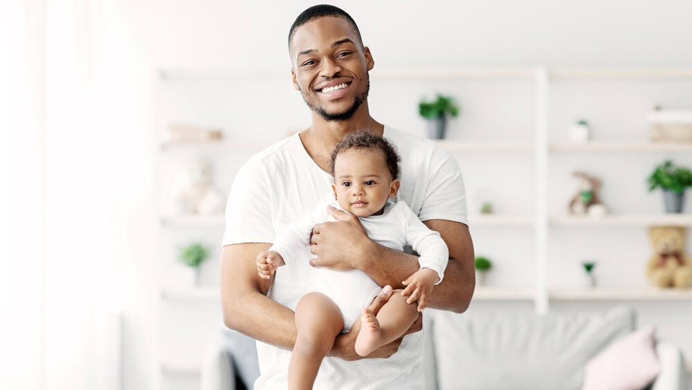 Fatherhood Concept. Portrait Of Happy Young Black Man Holding Cute Newborn Baby In Hands And Looking At Camera, Smiling Millennial Father Bonding With His Infant Child At Home, Copy Space