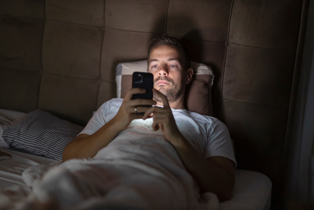 A tired man with insomnia watching online videos in dark bedroom at night.