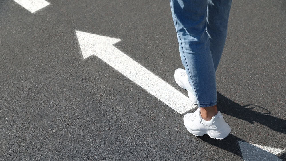 Woman walking on asphalt road with white arrows, closeup. Move forward