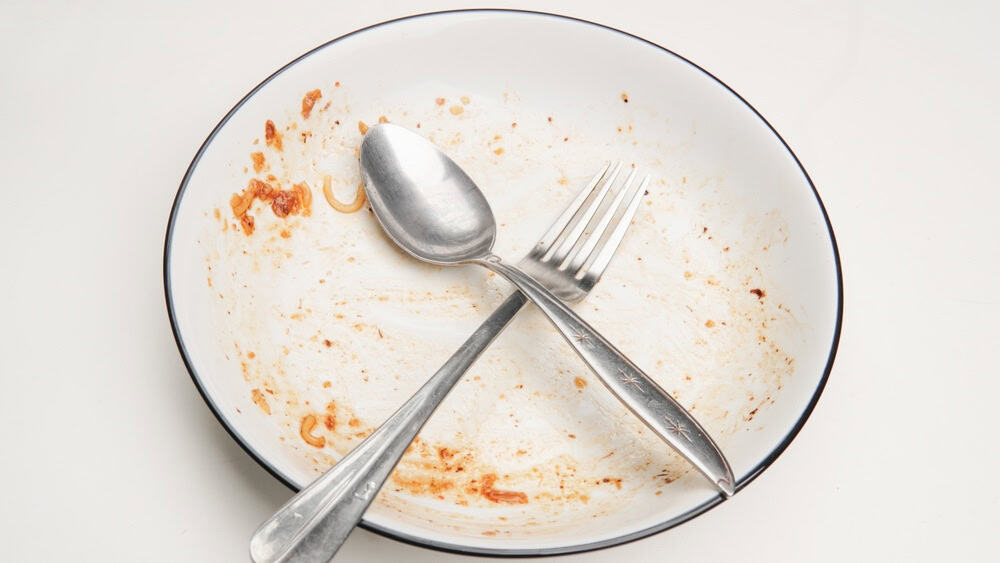 Dirty plate with spoon and fork arranged to form X. Photo can be used for the concept of how to clean the plate after food.