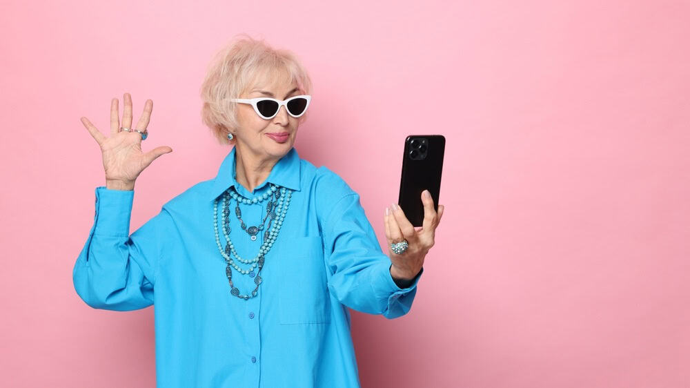 Cool grandmother taking selfie on pink background. Space for text
