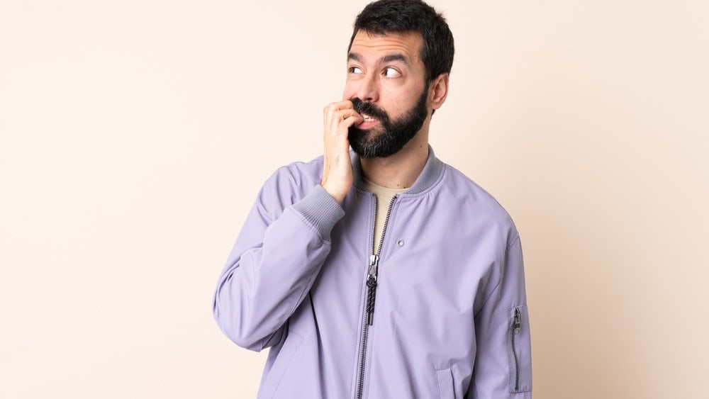 Caucasian man with beard wearing a jacket over isolated background is a little bit nervous