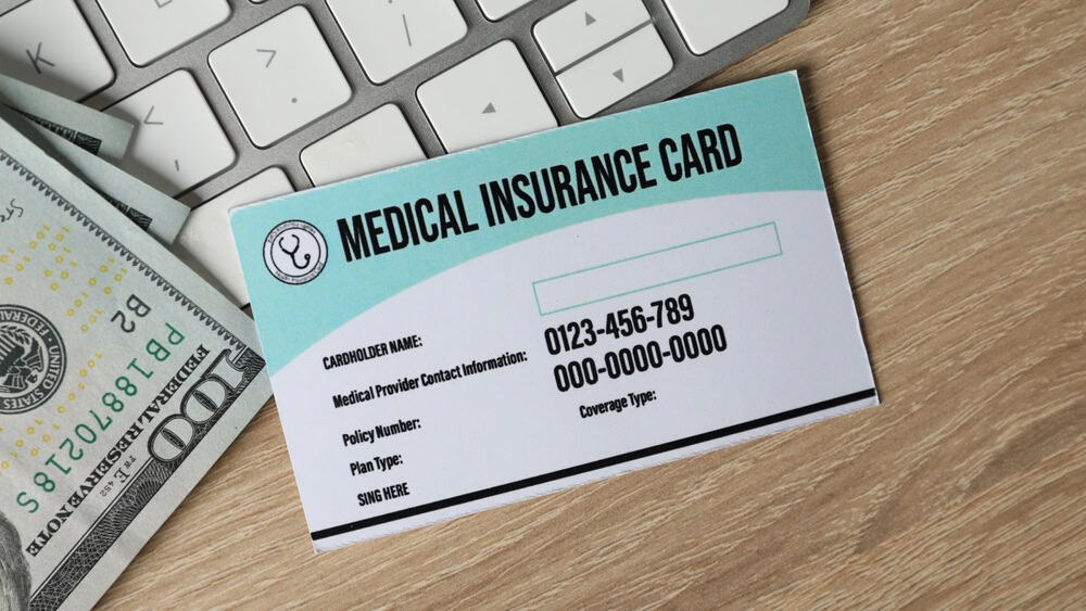 Medical insurance card, money and keyboard on wooden table, flat lay