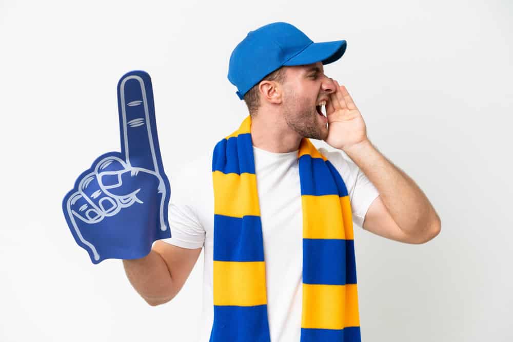 Young caucasian sports fan man isolated on white background shouting with mouth wide open to the side