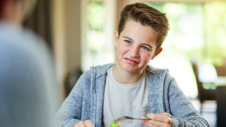 Upset, child and reject food at dinner table for eating vegetables and no to nutrition at home. Healthy, brussel sprout and face with disgust, refuse and fussy eater with balanced diet and salad
