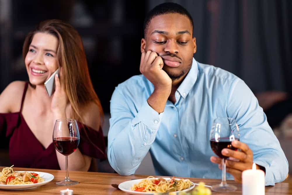Black Man Feeling Bored While His Girlfriend Talking On Cellphone During Date