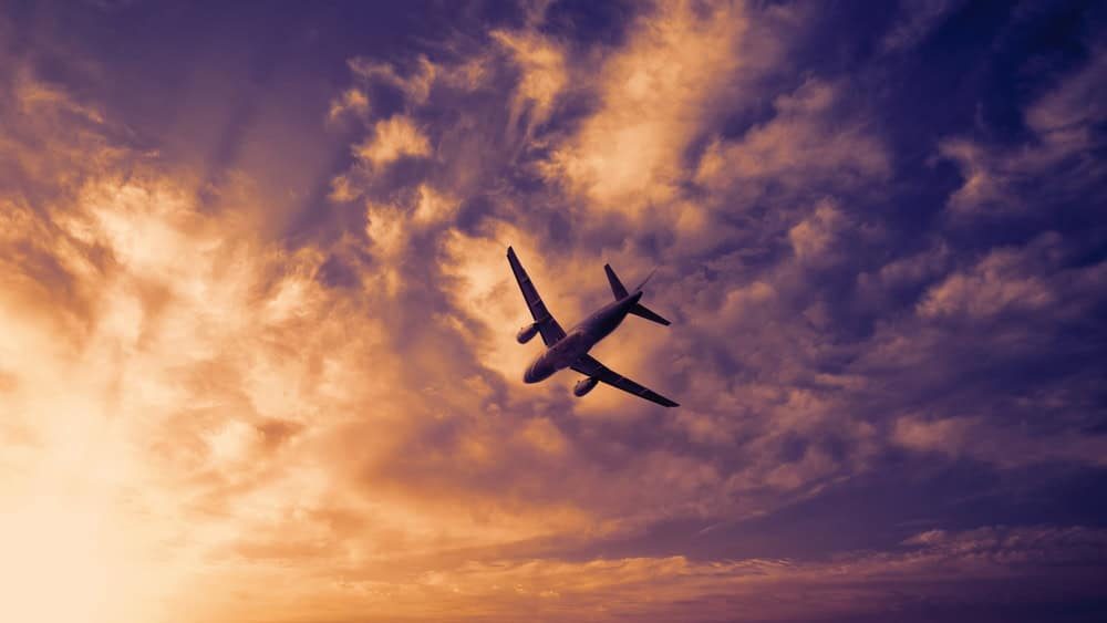 Airplane in the sky. Airplane in flight at sunset or evening sky. Commercial airliner silhouette in the colorful evening or night moon skies. Aircraft symbol of travel adventure global connectivity.