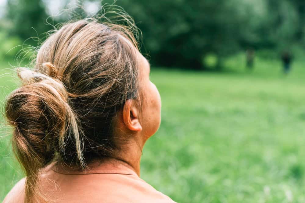 Mature woman enjoying nature in lush green field. Standing with her back to camera and looking at forest