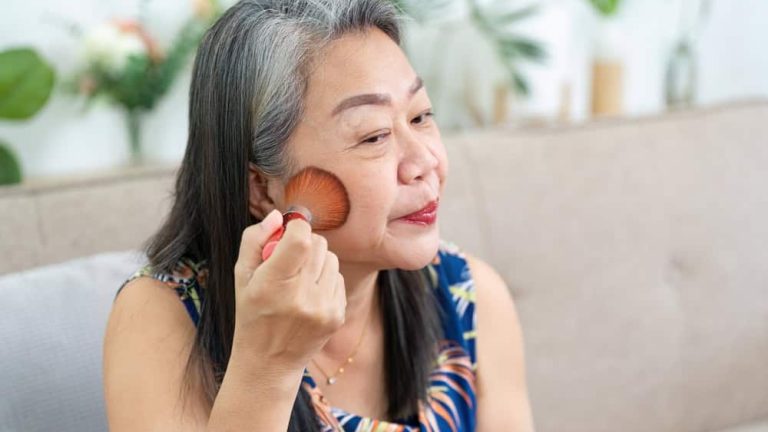 Makeup Application. Mature woman applying blush with a brush in front of a mirror.