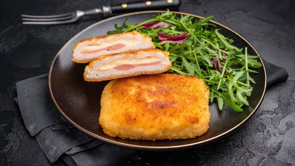 Chicken cordon bleu cutlet with cheese and ham on plate with salad. black background. top view.