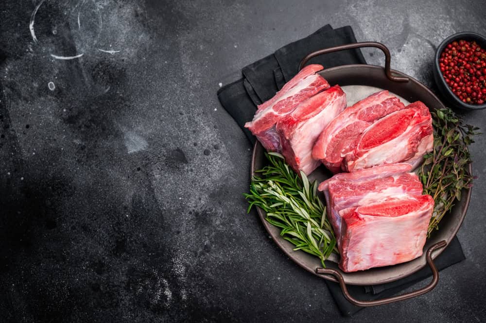 Raw Beef Short Rib, uncooked meat with bone and fat. black background. top view.