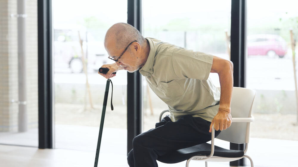 Elderly Asian man standing up with a cane
