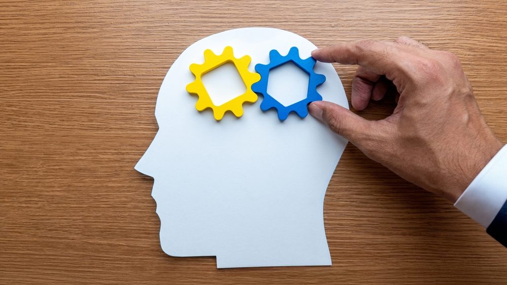Human head cutout with gears being adjusted by a hand. Change of mindset, transformation of thinking, innovation, and personal development concept.