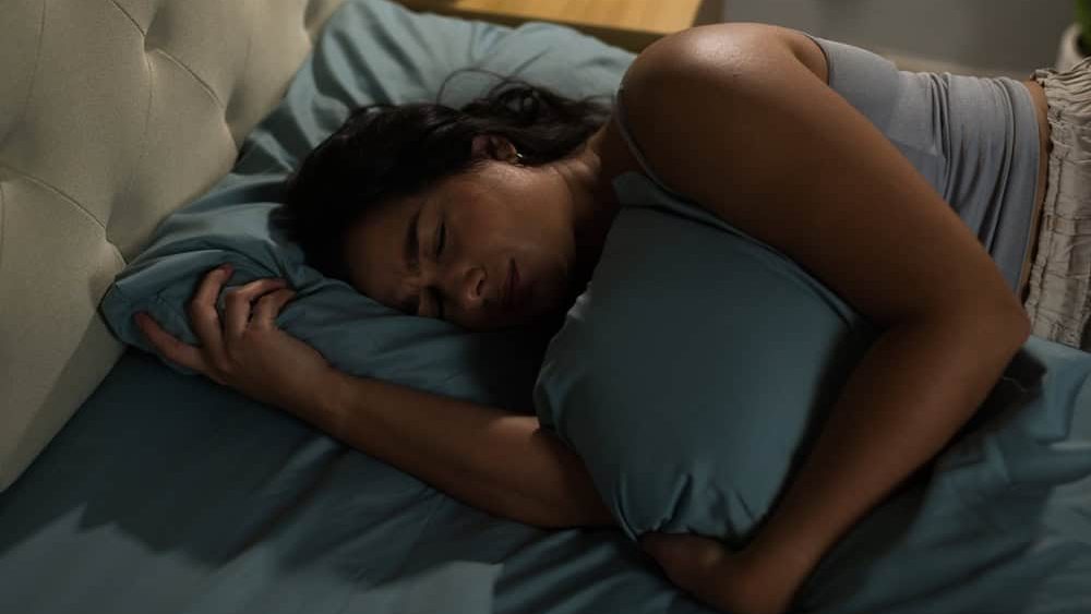 Distressed Hispanic woman is lying in bed and hugging pillow, having trouble sleeping after an argument or breakup