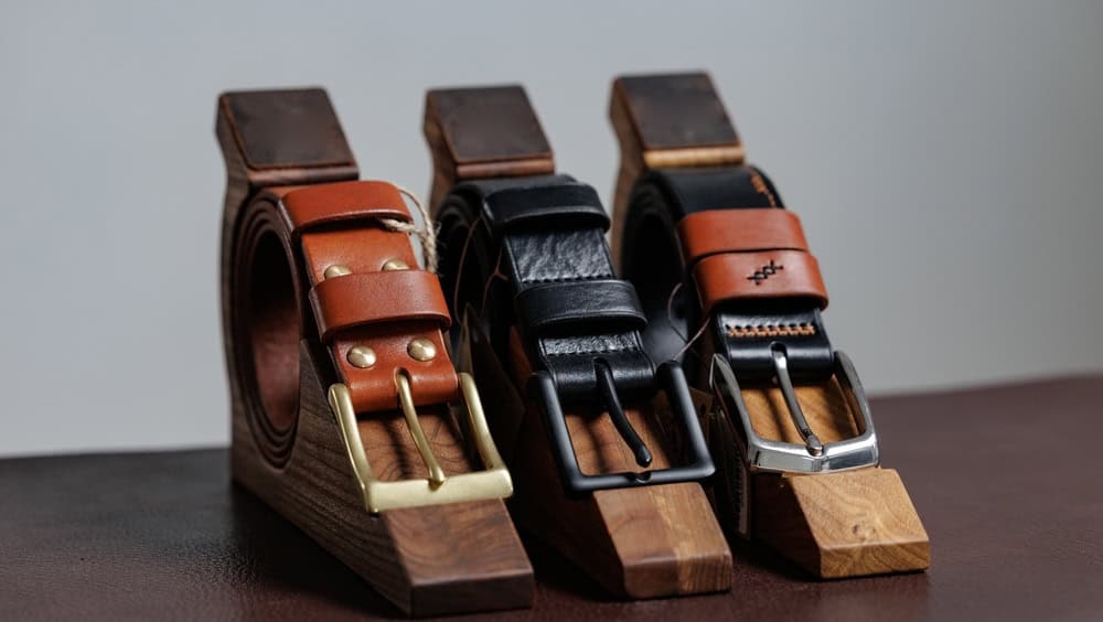 Handcrafted leather belts displayed on wooden stands.